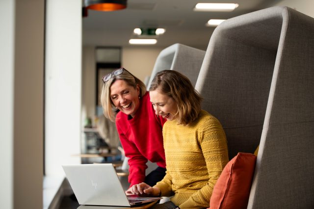image of two women looking down at a laptop smiling.
